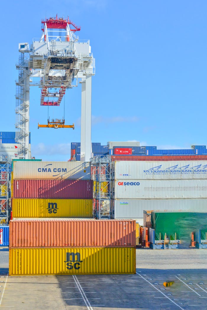 heros-img Stacked cargo containers in a sunny port industrial setting with crane.